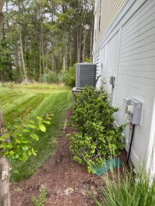 a back yard with a tree, bushes and an air conditioner