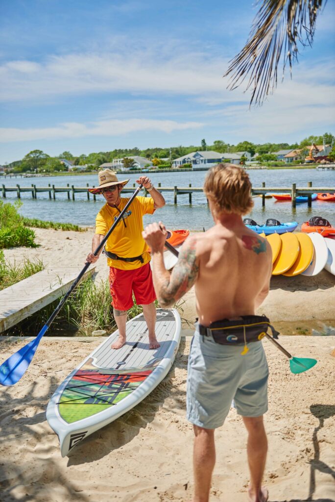 a man standing next to a man on a surfboard