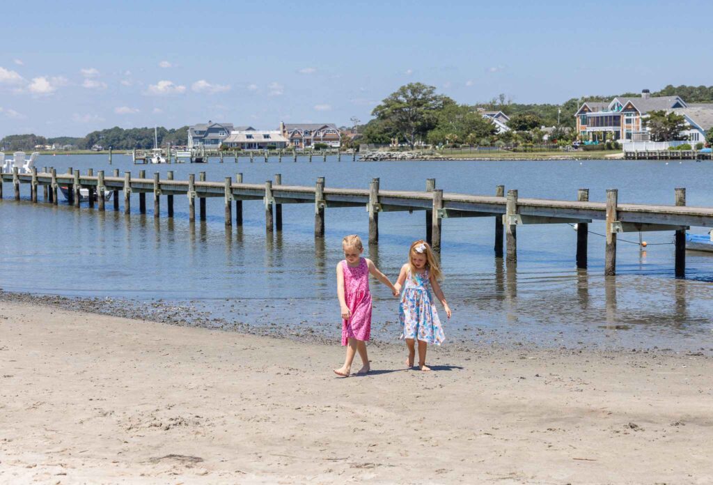 two little girls walking on a beach next to a pier