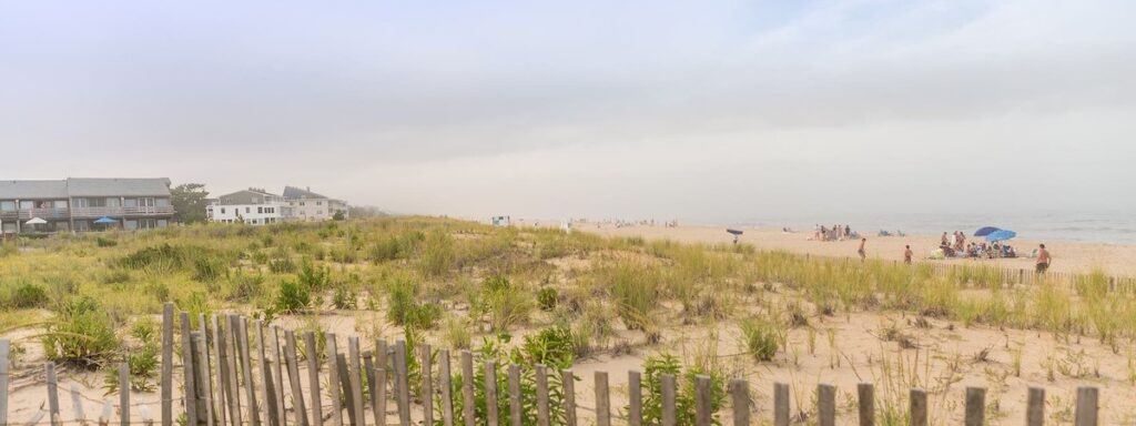 a sandy beach with a fence and houses in the background