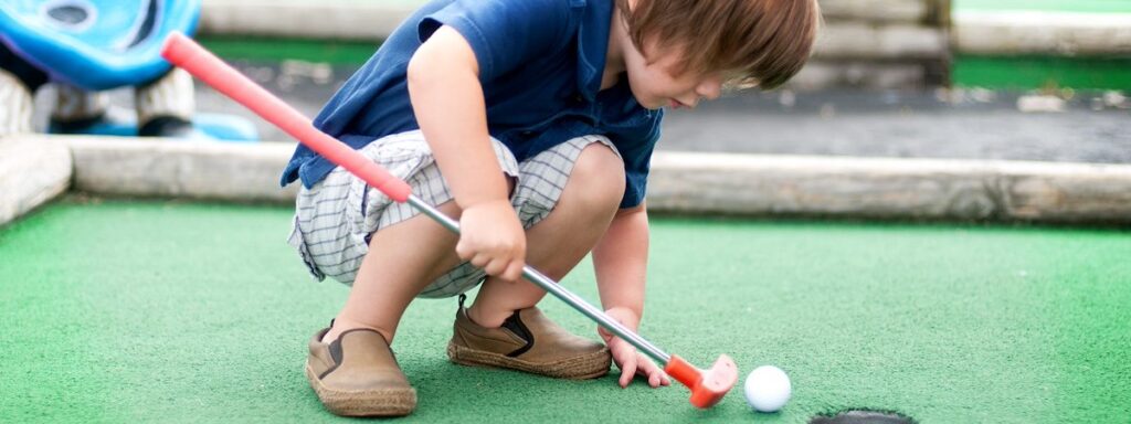 a little boy playing golf on a green court