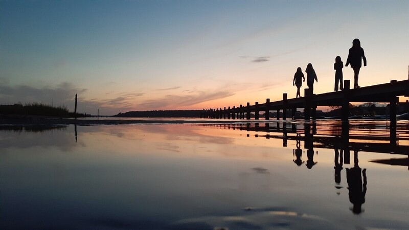 a group of people standing on a dock at sunset