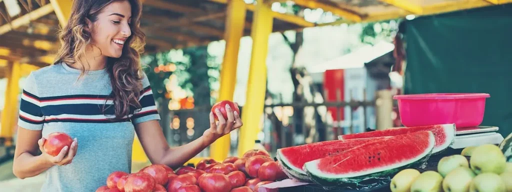 A woman picking up tomatoes from a farm stand