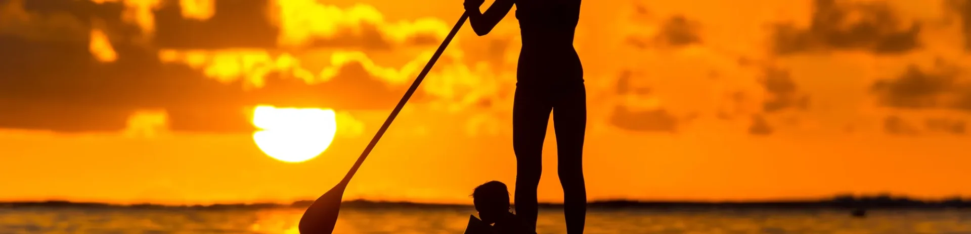A woman and her son paddle boarding during sunset.
