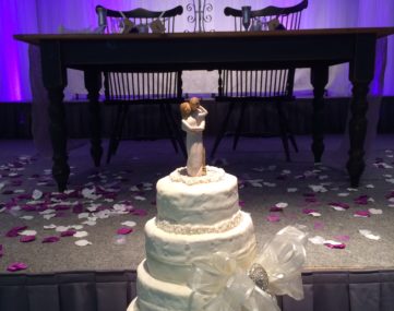 spotlight on wedding cake and table in front of wedding couple table on back lit stage