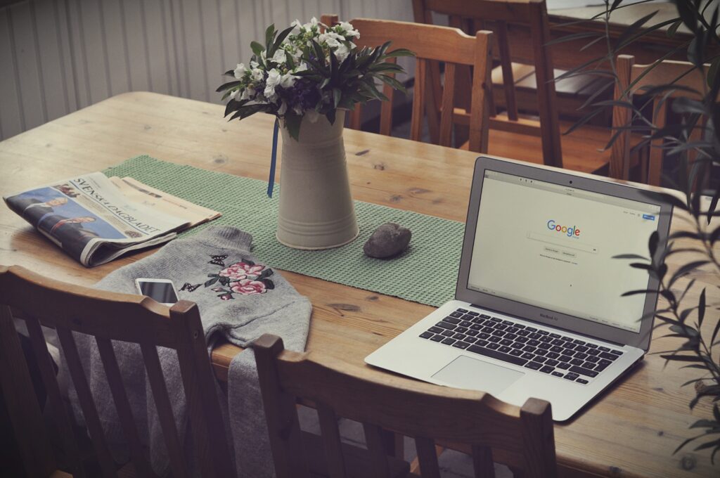 Laptop, flowers, newspaper, sweater and phone sitting on wooden table