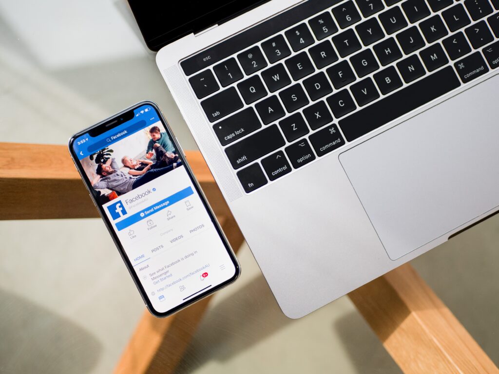 Cell phone displaying facebook next to macbook