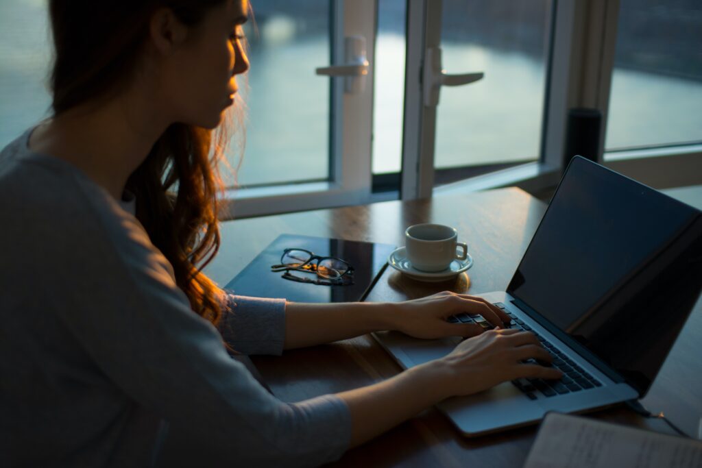 Woman types on laptop with coffee and glasses next to her