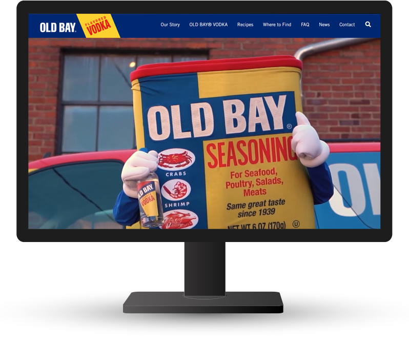 Old bay mascot poses with old bay vodka on monitor