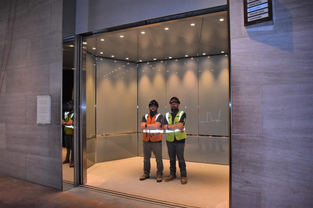 two men in safety vests standing in front of a glass wall