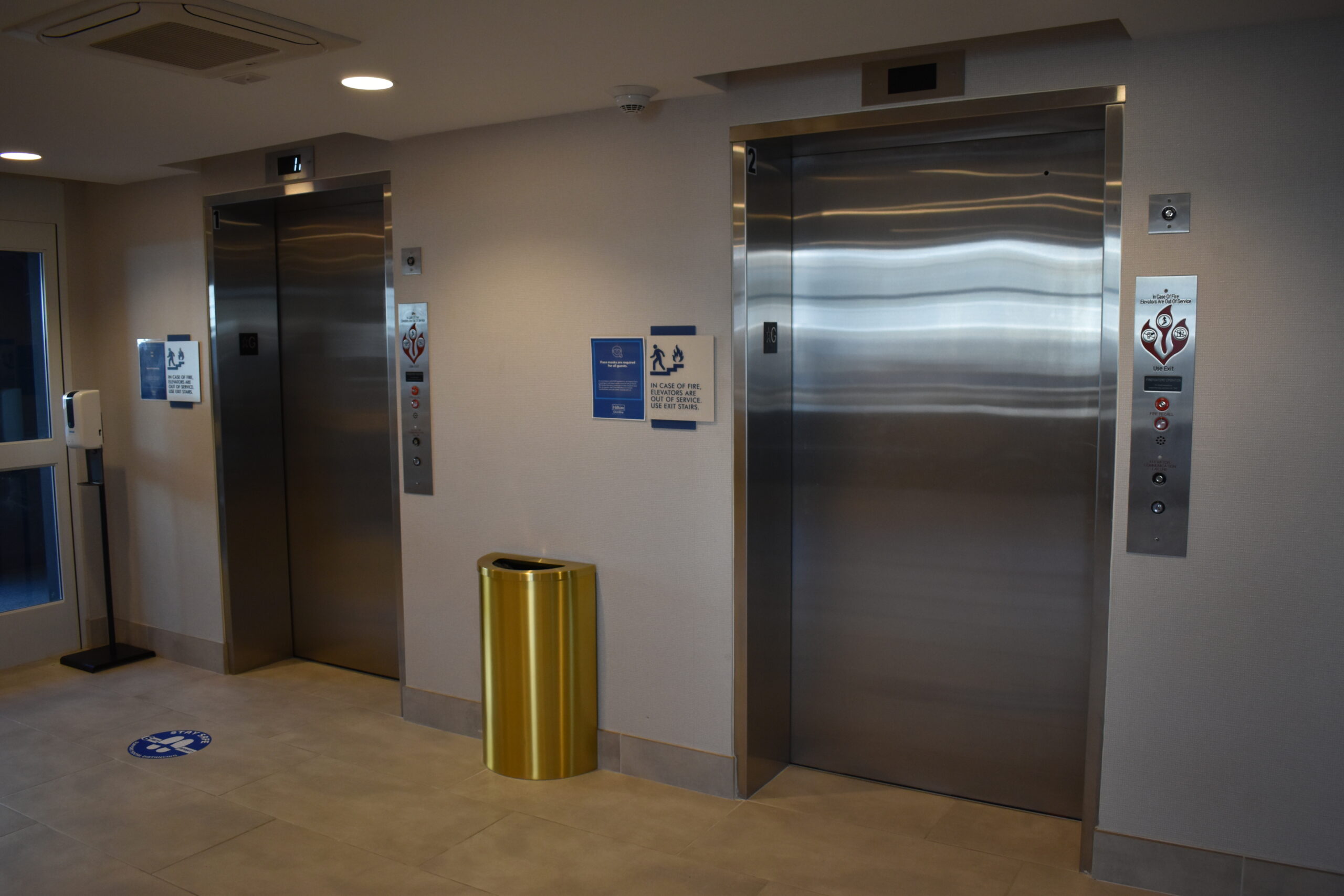 an empty room with two elevators and a yellow trash can
