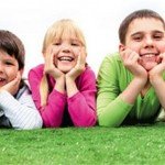 Three kids pose laying in the grass