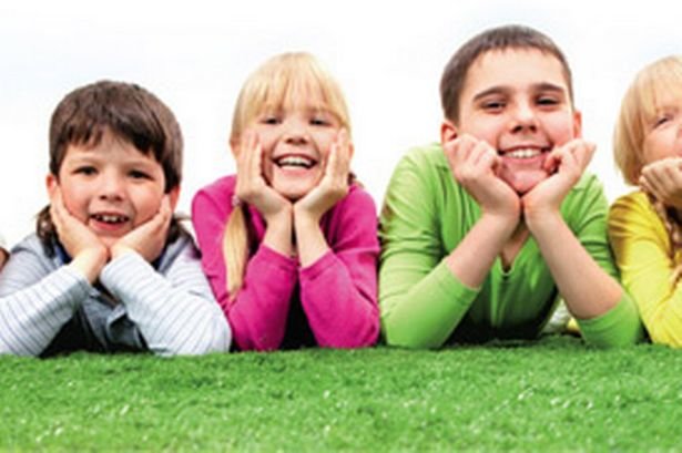 Three kids pose laying in the grass