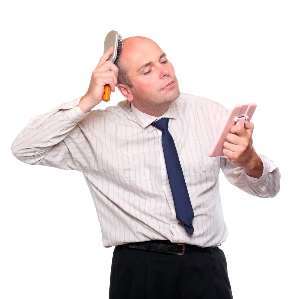 A bald man brushes lack of hair while looking in hand mirror