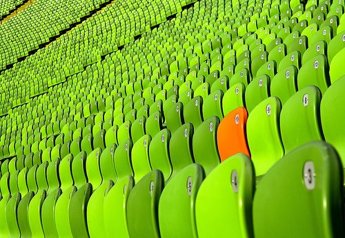 Bleachers filled with green chairs and one orange chair stands out
