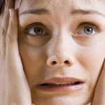 Woman holds hands to face with anxious and scared look