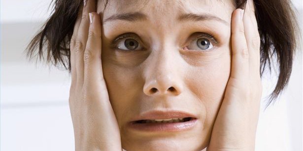 Woman holds hands to face with anxious and scared look