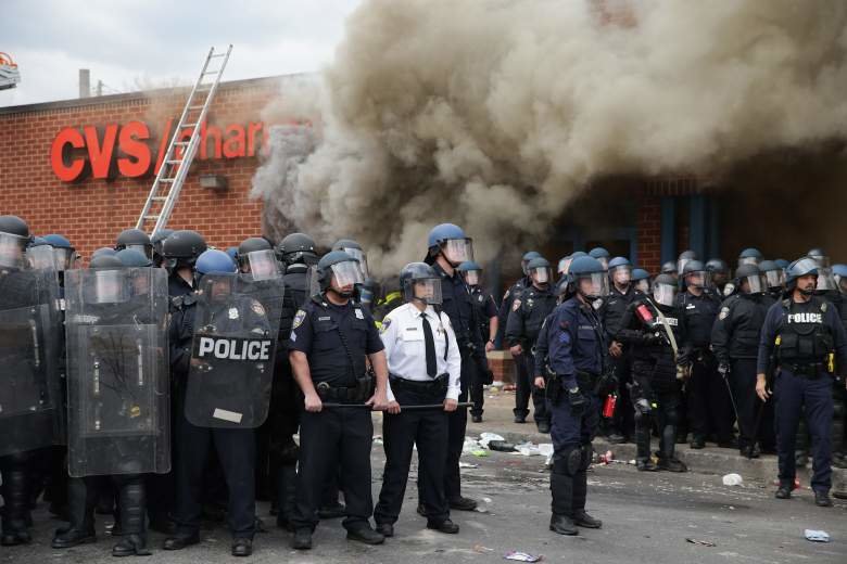 Police personnel line up protected with shields in front of CVS building with smoke in background