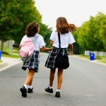 Rear view of two school girls walking down street holding hands