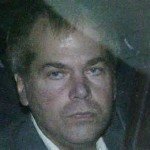 John Hinckley in the back of a cop car with angry expression