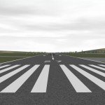 View of an airport runway going into the distance with surrounding green fields