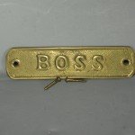 Gold plated sign reads BOSS with screws sitting in front of sign