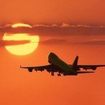 Airplane flying off toward orange sunset filled sky