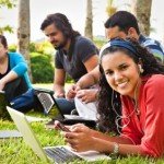 Four young adults sit on grass with computers and smartphones