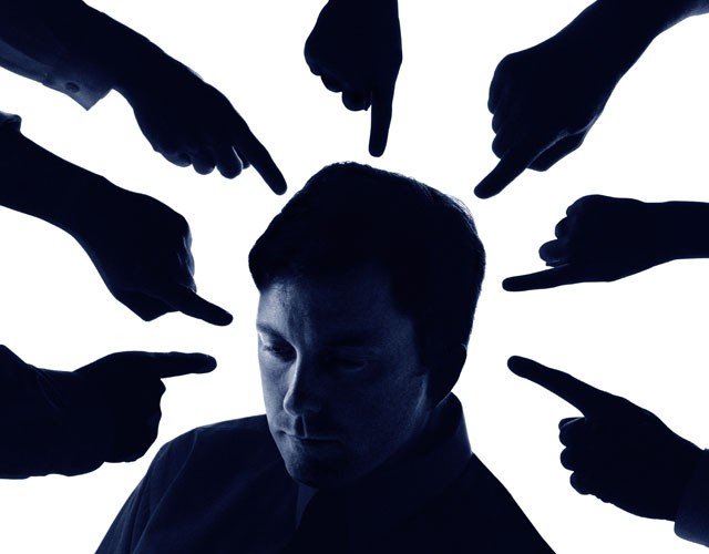 Man looks sad as seven hands point fingers at his head