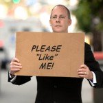 Man in suit holds cardboard sign that reads Please Like Me!