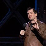Comedian Jim Jeffries in brown leather coat performs live