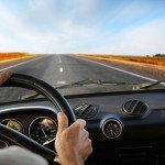 Man behind steering wheel driving on long road