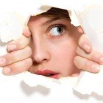 Woman peeps through cracked hole with anxious look
