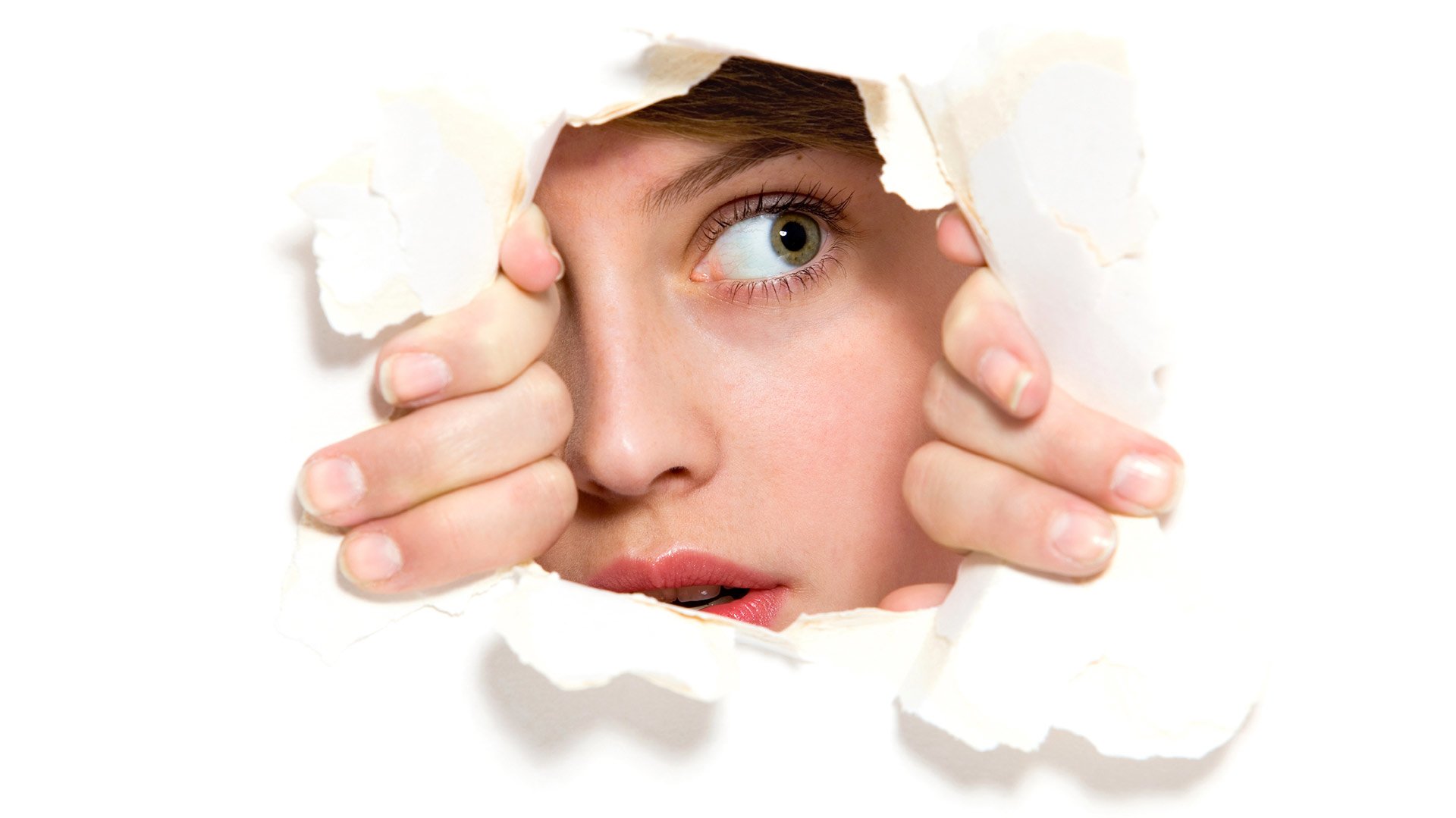Woman peeps through cracked hole with anxious look