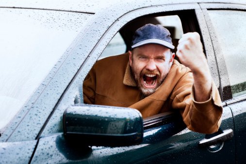 Man clenches fist with angry look while in car