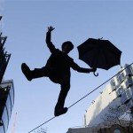 Man wearing tophat with umbrella walks on tightrope