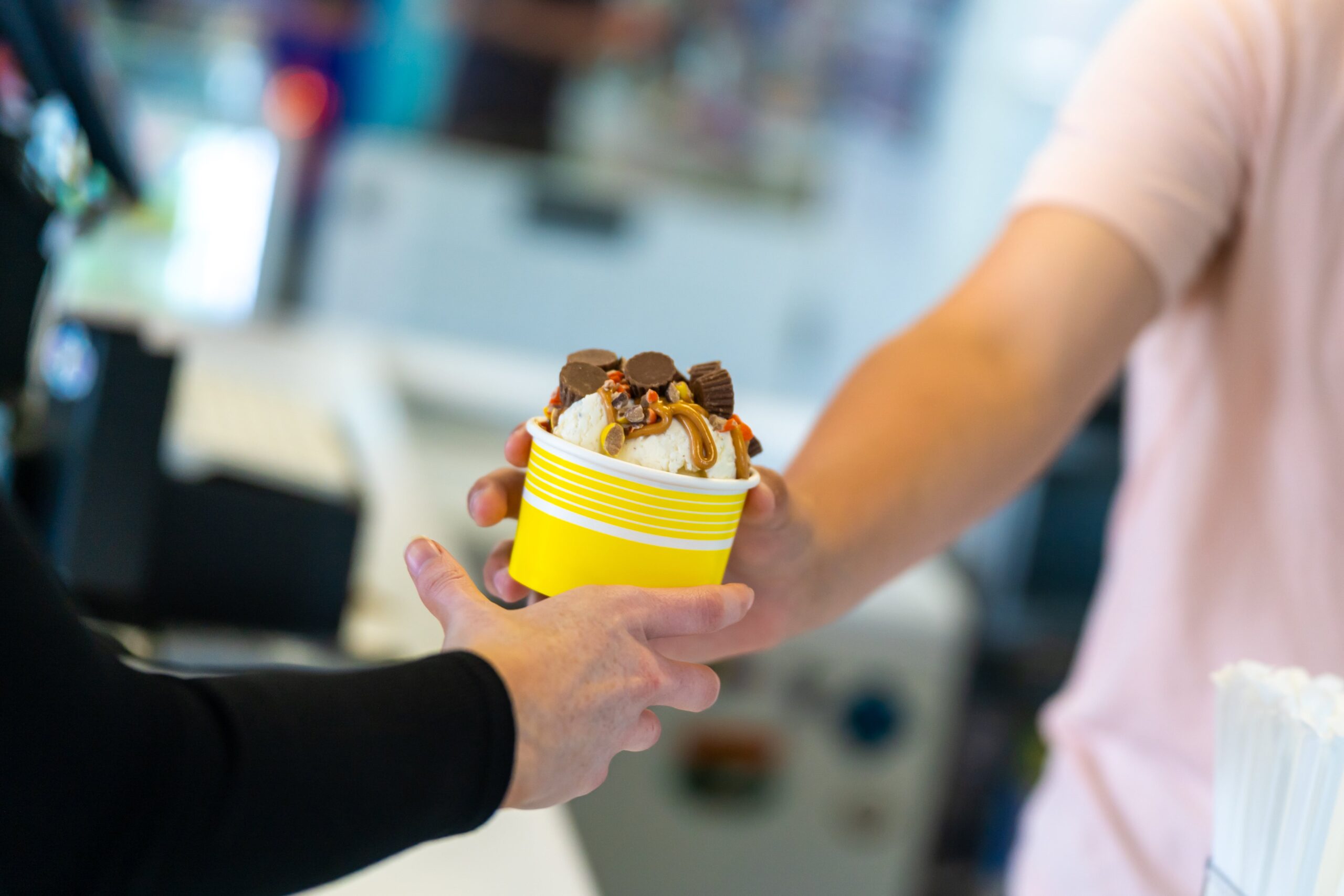 A worker handing a customer a cup of ice cream.