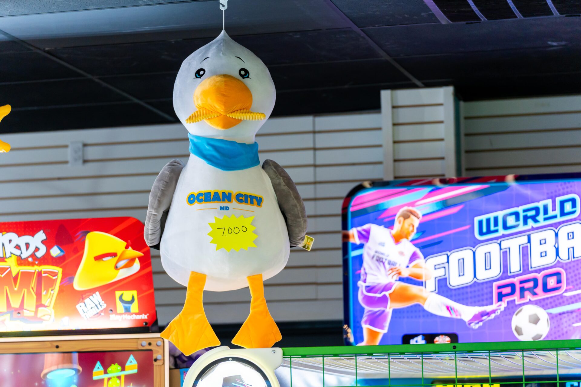 A seagull stuffed animal hanging from a shelf at an arcade.