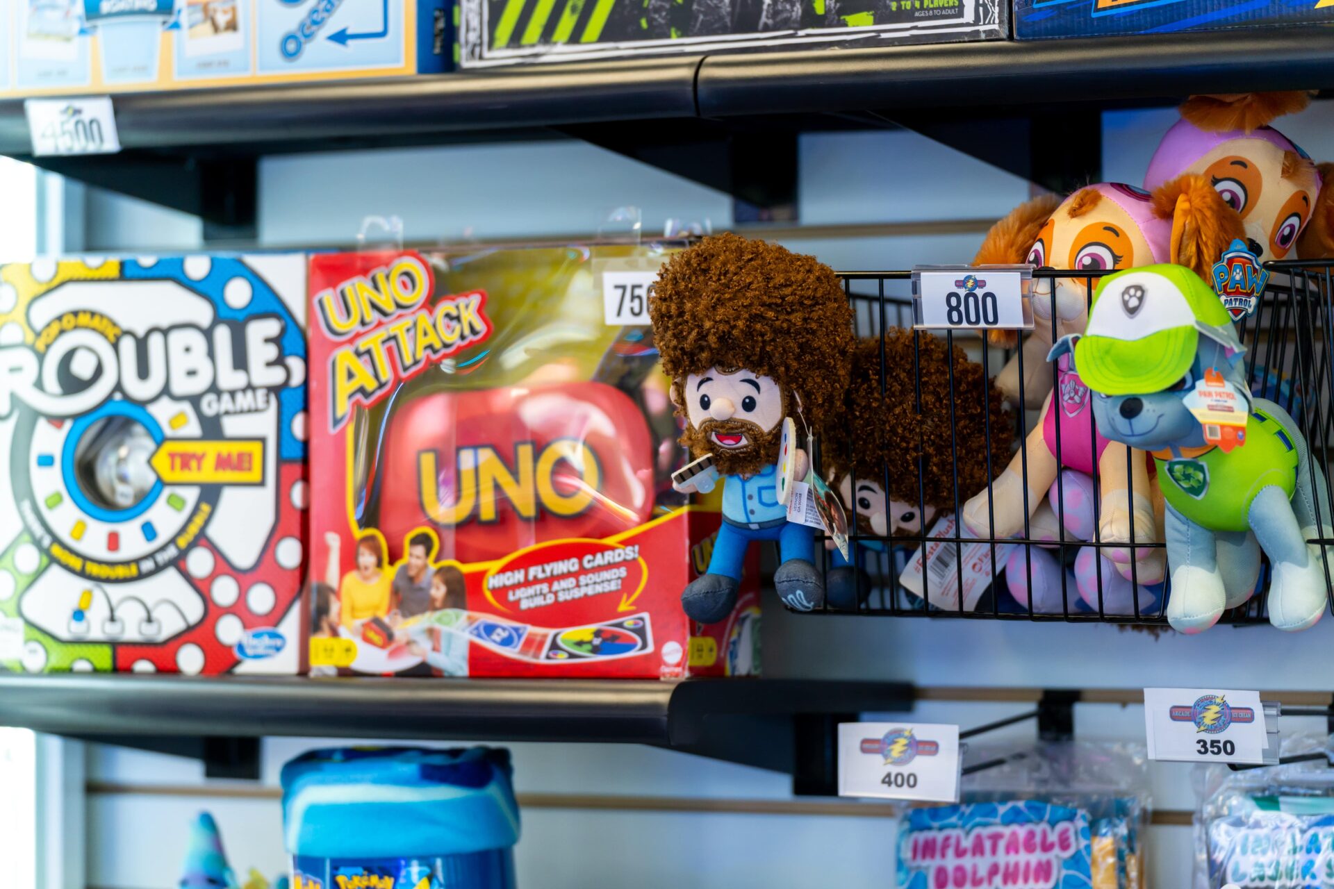 Arcade prizes on a shelf including stuffed animals and an uno game.