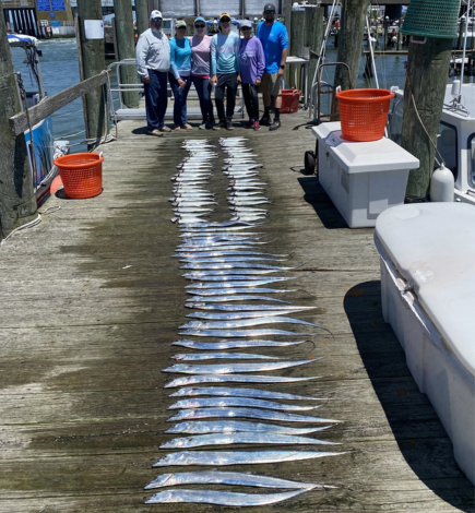 Men and women standing on the dock beside all the fish they caught