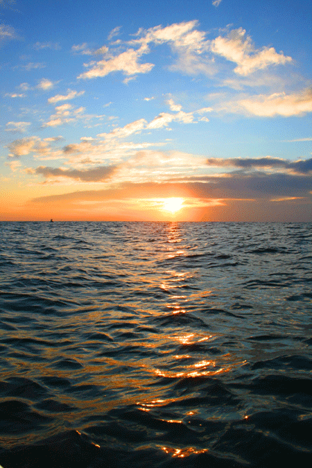 Sun rising over the ocean under a slightly cloudy, blue sky in Ocean City MD