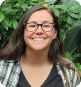a woman wearing glasses standing in front of green plants