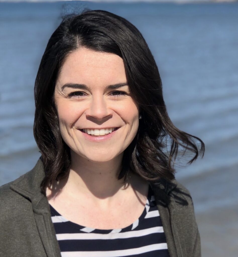 a woman standing in front of the ocean smiling