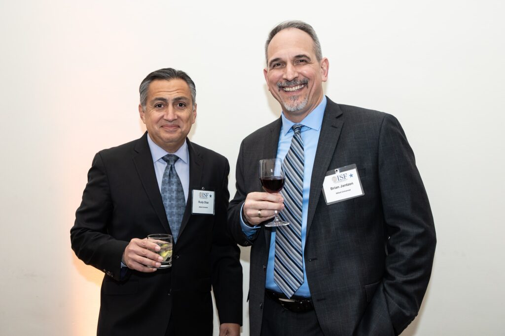 two men standing next to each other holding wine glasses