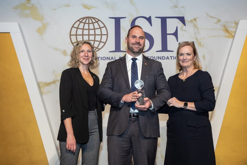 three people standing in front of a wall holding an award
