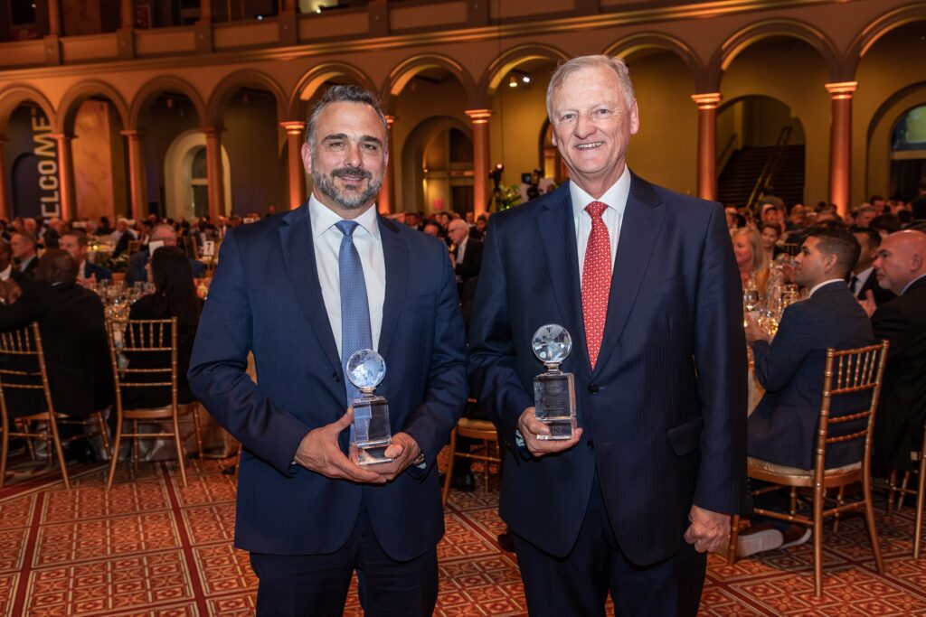 two men standing next to each other holding trophies