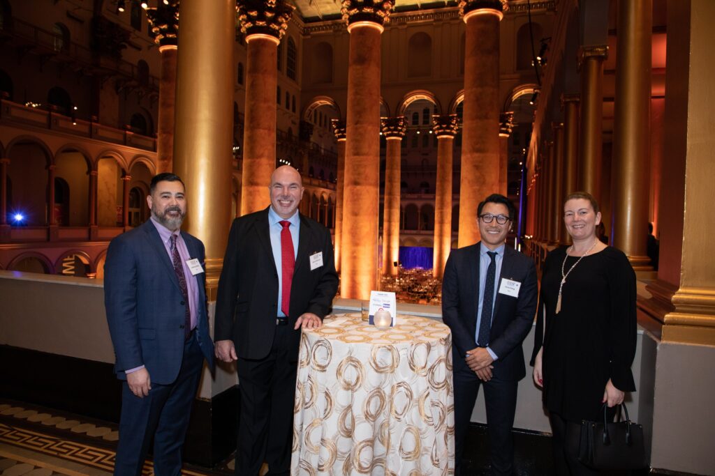 four people standing in front of a table with a cake on it