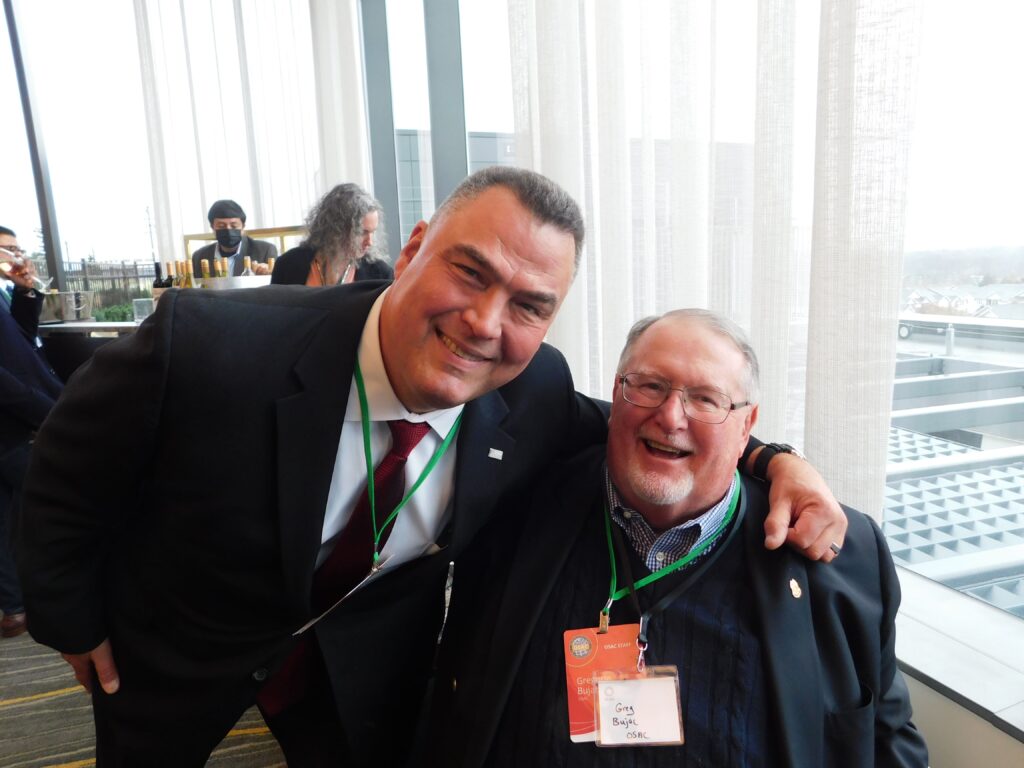 two men standing next to each other in front of a window