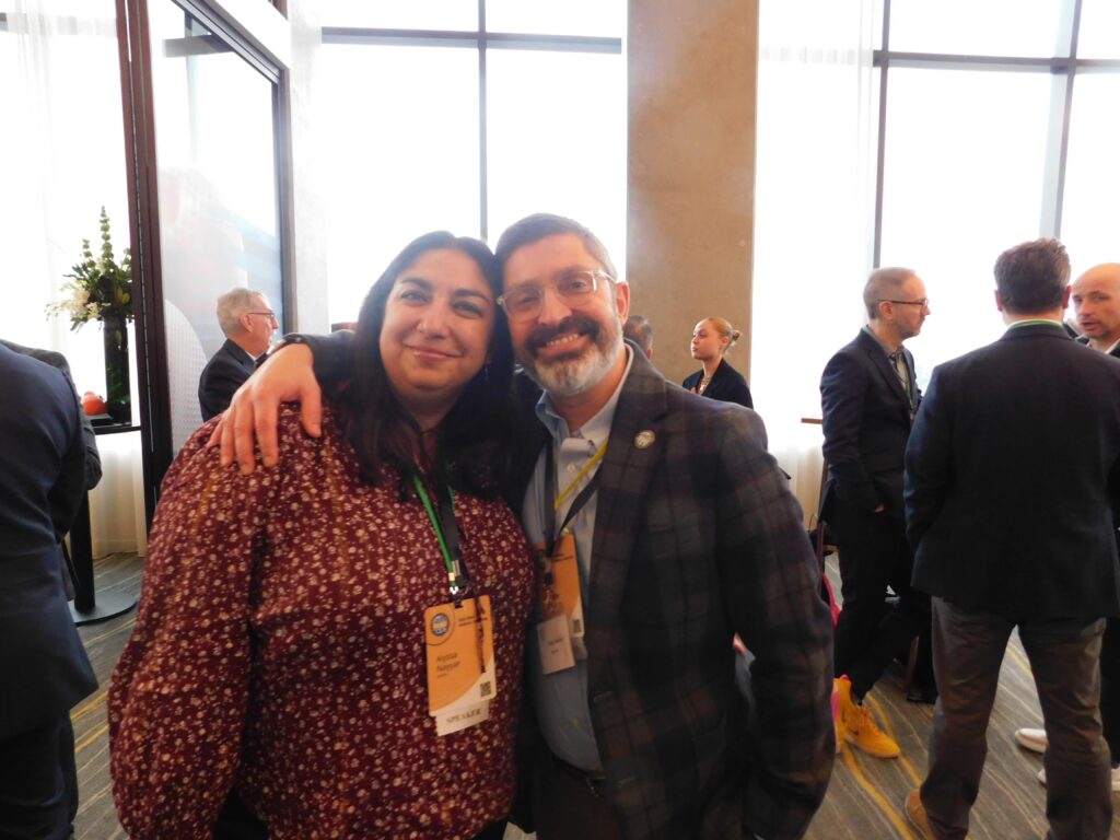 a man and woman posing for a photo in front of large windows
