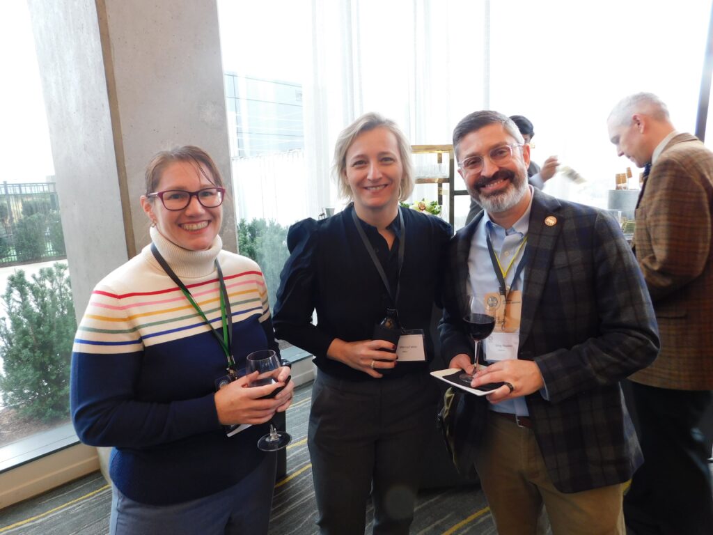 three people standing next to each other holding wine glasses